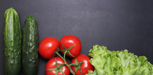 Fresh green cucumbers and red ripe tomatoes. Vegetables on a black textured background.
