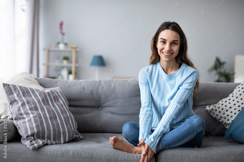 Wall mural relaxed smiling woman sitting on sofa at home.