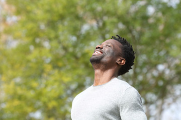 Happy black man breathing deeply fresh air in a park