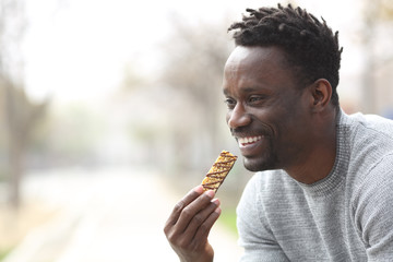Happy black man eating a cereal bar in a park