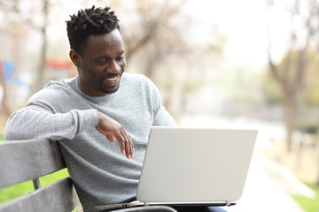 Happy black man using a laptop in a park