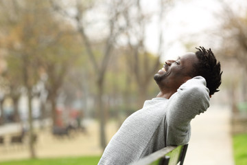 Happy black man relaxing on a bench in a park - obrazy, fototapety, plakaty
