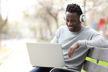 Happy black man watching media on laptop with headphones