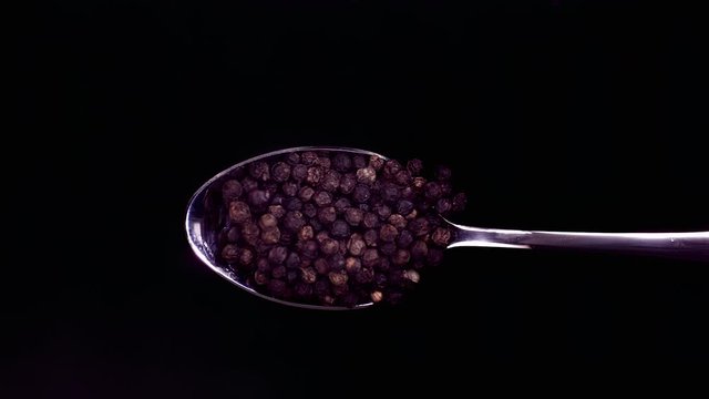 A Full Spoon Of falling peppercorns down on black background closeup in super slow motion
