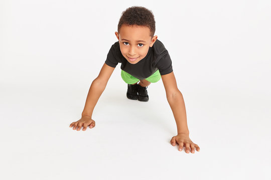 Fitness, activity, health and well being concept. Isolated image of strong athletic cute dark skinned boy standing in plank with arms extended, doing push ups for building upper body strength