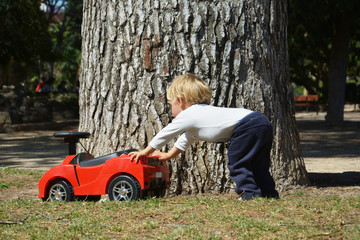 Blond boy playing with his red toy car