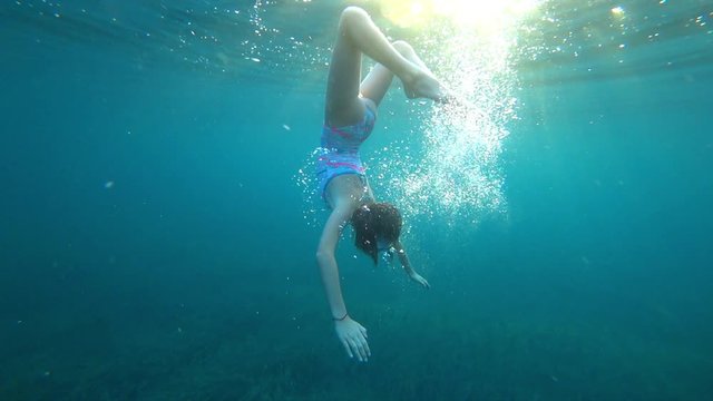 Beautiful girl swimming under the ocean's surface with air bubbles and sunlight, active healthy fitness lifestyle. 