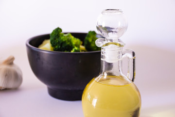 Olive oil in a jar and some vegetables behind on white background