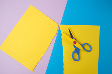 abstract background of colored paper, yellow stripes with a zigzag end and plastic scissors