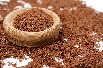 isolated heap of flax seeds lies on a white background and in a light brown ceramic bowl