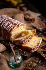 homemade rectangular sliced pound lemon cake with white glaze on top on wooden board on rustic table with sackcloth, lemon slices, vintage forks