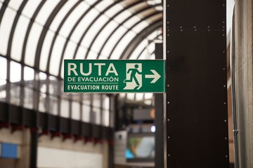 Emergency exit evacuation route sign in Spanish language at an airport in Colombia. The text reads Evacuation route in Spanish and English