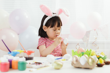 toddler girl  painting  Easter eggs at home against white window background