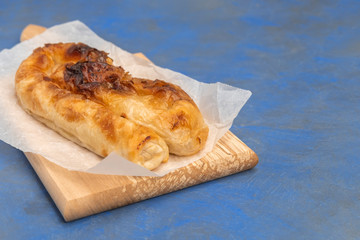 Traditional Bulgarian cheese pastry Banitsa on wooden board on dark blue background, copy space