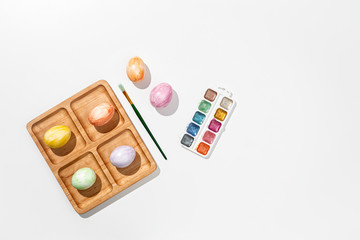 Easter holidays concept. Colorful Easter eggs, wooden stand, paints  and paintbrush. White background. Top view.