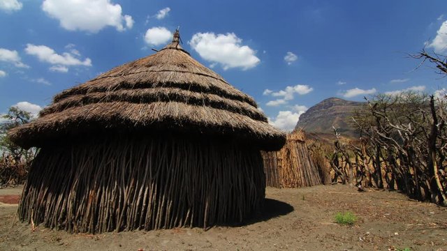 Time lapse of clouds passing over grass hut in Africa