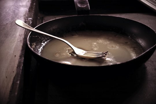 dirty frying dripping pan with used fat and fork
