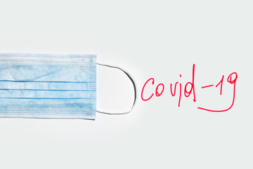 Close-up of medical flu mask near text covid-19, isolated on white background.