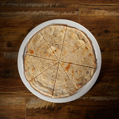 Flatlay of Italian pizza on wooden background. Large pita cut into pieces.  Healthy bread. Cutting knife. Basis for pizza. Preparation for pizza