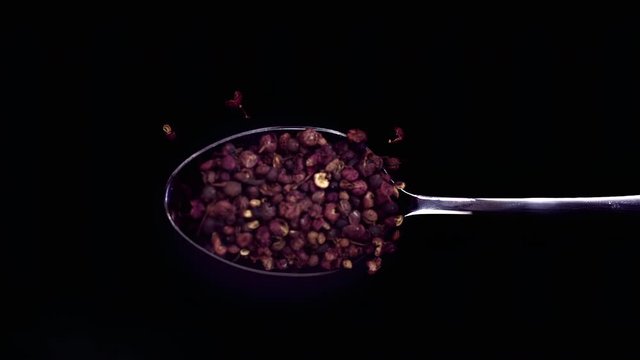 A Full Spoon Of falling Sichuan pepper down on black background closeup in super slow motion