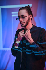 Young adult male posing in bright neon studio, looking calm and casual, dressed in black with sunglasses. Vertical photo