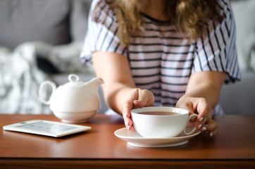 Cozy home interior with teapot and woman holding cup of tea.