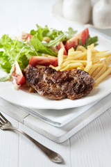 Grilled Steak with french fries and fresh salad. White wooden background.