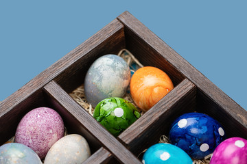 Different easter eggs in a box with straw on blue background