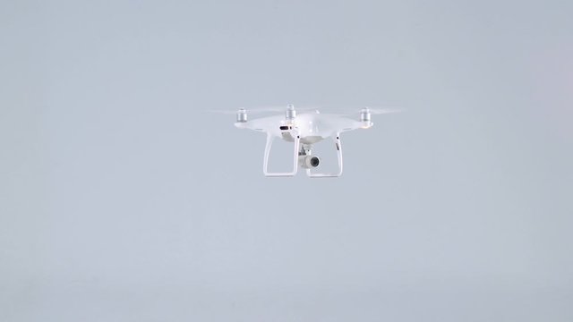 Active small white unmanned quadrocopter drone with action camera flying turning around at studio