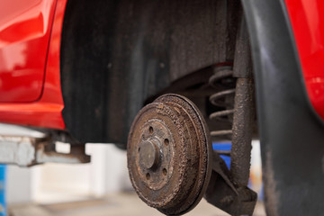 Rusty drum brakes, rear on red car. Change the old to new brake disc on car in a garage. Auto mechanic repairing