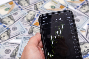 A stock forex exchange rate of us dollar on a smartphone screen, banknotes on background