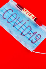 Coronavirus - COVID-19. Test tube with blood identified by the COVID-19 coronavirus on red background. Protective medical mask and test tube. Copy space