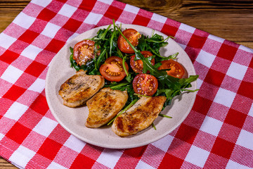 Roasted chicken breasts and salad with arugula and cherry tomatoes in a ceramic plate