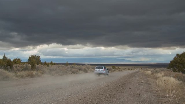 Car driving on dirt road kicking up dust on stormy day with dark dramatic clouds in the sky.