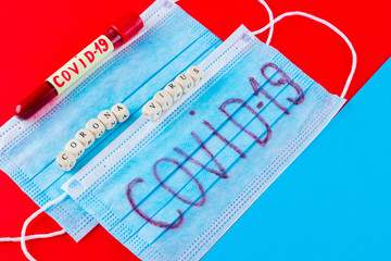 Coronavirus - COVID-19. Test tube with blood identified by the COVID-19 on blue red background. Protective medical mask and test tube. Word "Coronavirus" made with wooden cubes