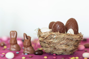 Bird nest with chocolate easter eggs and chocolate bunny on table