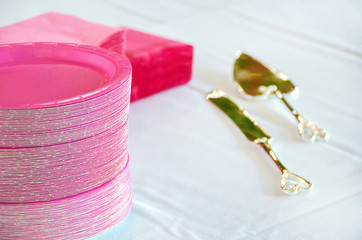 stack of pink wedding paper plates with napkins and gold flatware on white linen tablecloth
