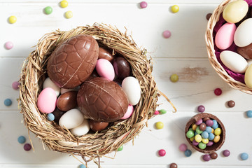 Top view of bird nest with chocolate eggs and easter almonds and sweets on white wooden table