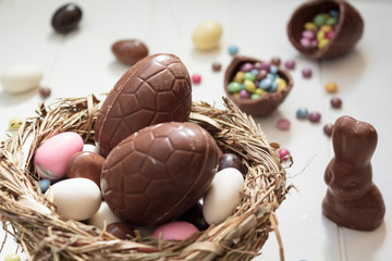 Delicious Chocolate eggs and easter almonds on nest, chocolate bunny and sweets on white wooden table