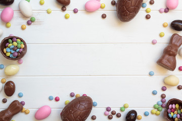 Top view of chocolate eggs, chocolate bunny, easter almonds and sweets on white wooden table with copy space. Easter frame composition