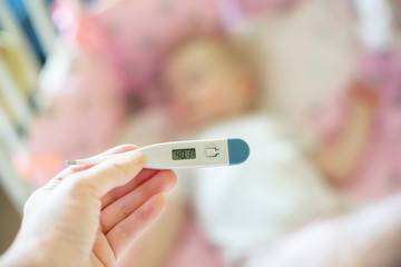 Fototapeta premium Close-up medical thermometer, Parent measuring temperature of ill kid, 1 years old toddler girl gets high fever lying on bed. fever in child