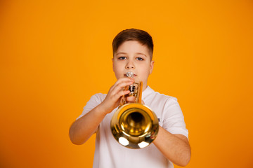 A boy plays the trumpet. A handsome teenager boy in a white T-shirt plays trumpet musical instrument