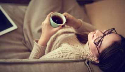 Fototapeta na wymiar A woman smiling as she holds a cup in her hands while she sits on the couch looking to the side