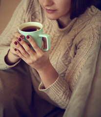 Happy young woman sitting on sofa holding a mug at home in the living room