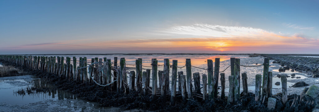 An impressive panorama view of the dike foreland near the imposing Eider barrage, Sunset over the the Wadden Sea, mudflat, tideland on the Northsea Wesselburenerkoog