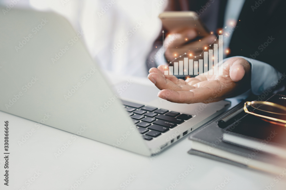Fototapete Business man in black suit sitting and working on computer and mobile phone. Man hands showing business growth and success result in virtual chart diagram with future growing plan.
