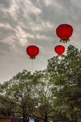 Obraz premium Guilin, China - May 10, 2010: 3 small red hot air balloons with candle inside float above green trees under dark cloudscape.