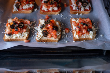 Young female chef in kitchen at home preparing mozzarella salami tomato and olives sandwiches. Healthy eating