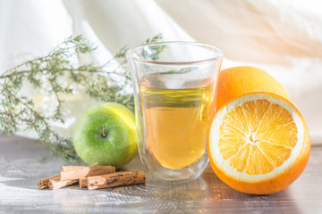 Vitamin lemon yellow tangerine peel drink in a transparent glass. Cinnamon and sliced orange on a wooden table. Juniper sprig apple