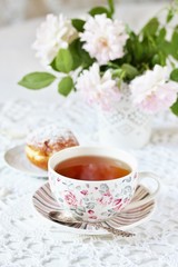 A tea party  in the style of Shabby Chic. tea in the beautiful tea steam with a pattern "rose". Delicate pink roses in a vase, white kettle in retro style. On a white lace tablecloth. Soft focus.